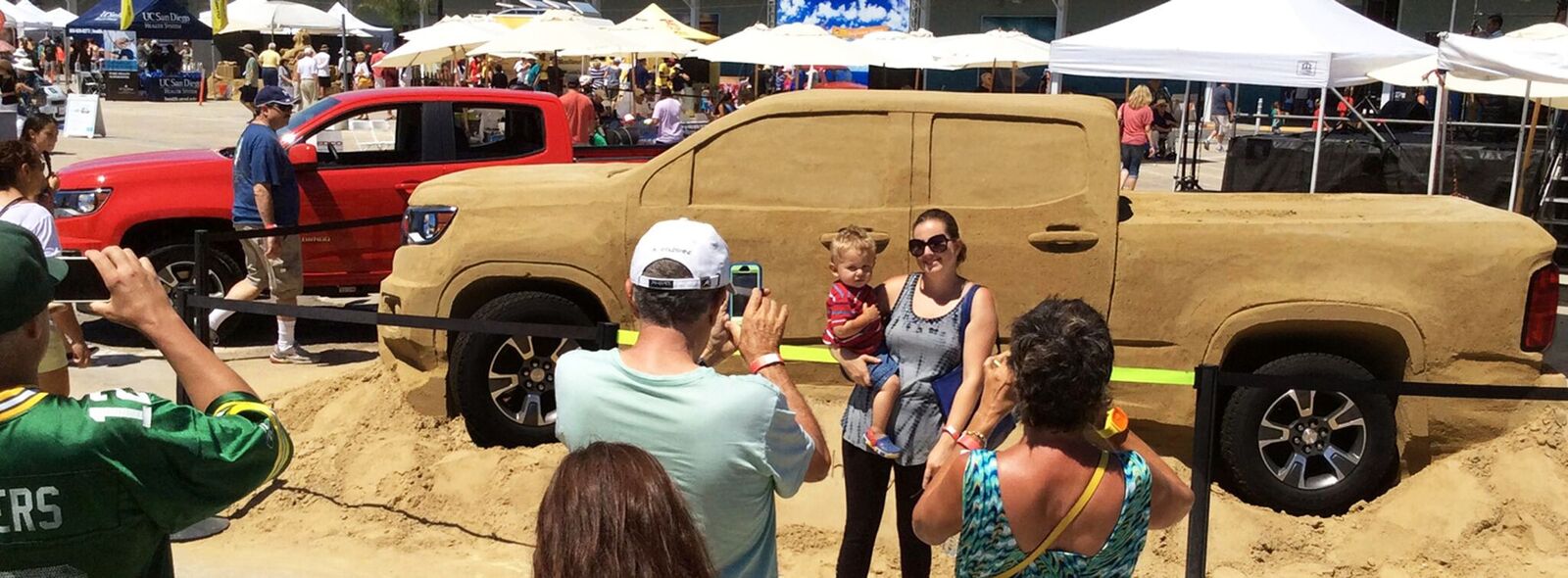 a man taking a picture of a woman with her child in a car sand sculpture