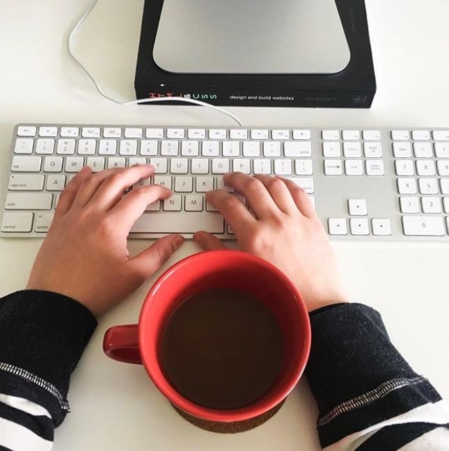 hands typing on the computer keyboard with a cup of coffee in the middle