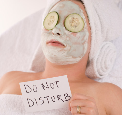 woman with facial mask and cucumber slices and and holding a note not to disturb