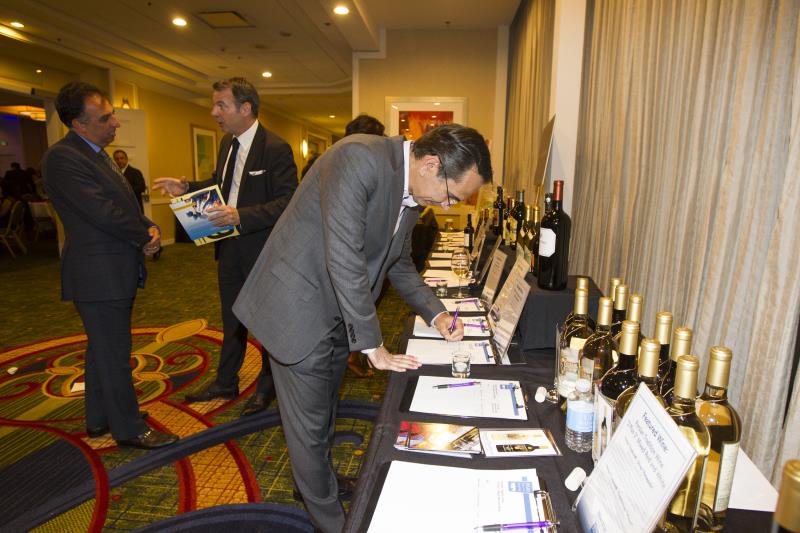 a photo of a man registering for a silent auctions event with two men talking at the back