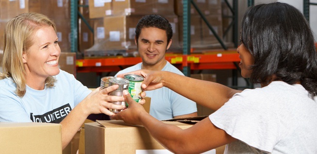 three volunteer people packing canned goods smiling at each other