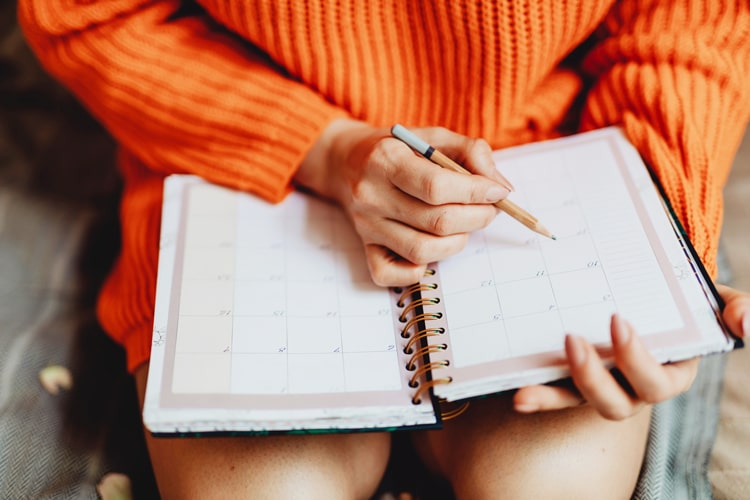 a woman wearing orange dress sitting and holding a pencil and writing notes