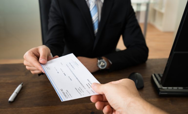a man wearing business attire and watch is paying to an employee by bank check