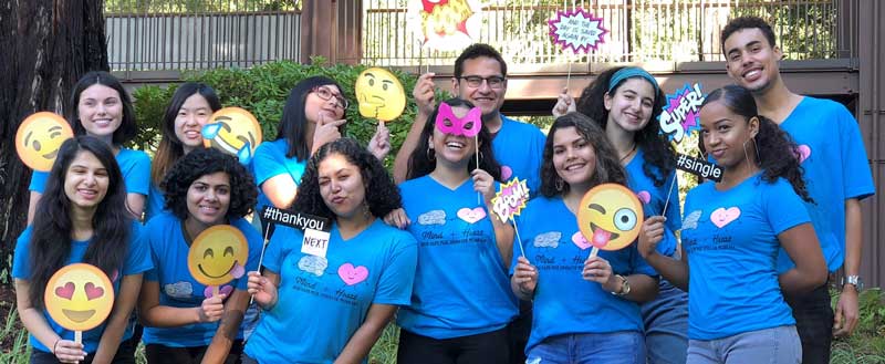 students wearing blue shirts are smiling and holding emojis for a photo