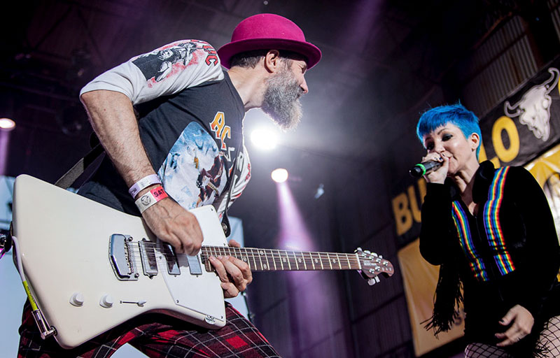 a man carrying an electric guitar with a woman singing