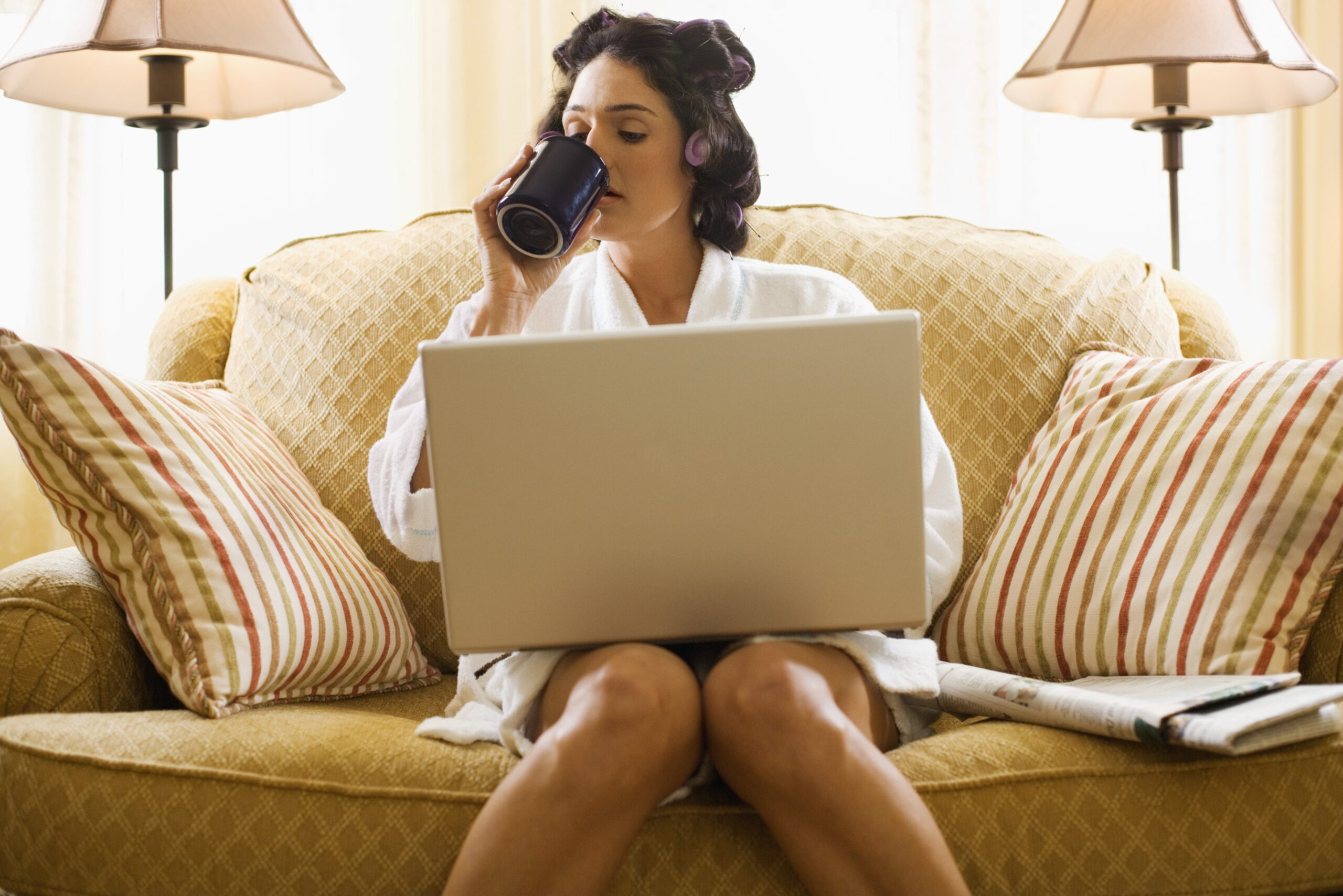 woman drinking while holding her laptop sitting on sofa