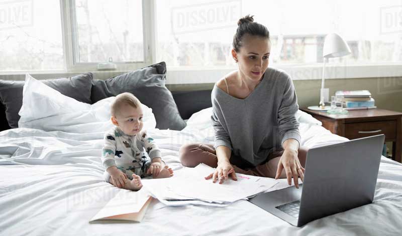 mother with her child working on laptop in bedroom at home