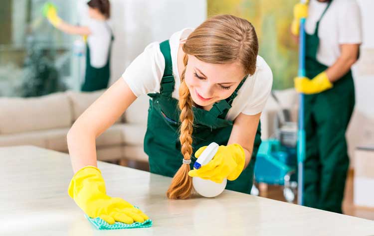 young happy woman wearing yellow gloves cleaning table with spray bottle