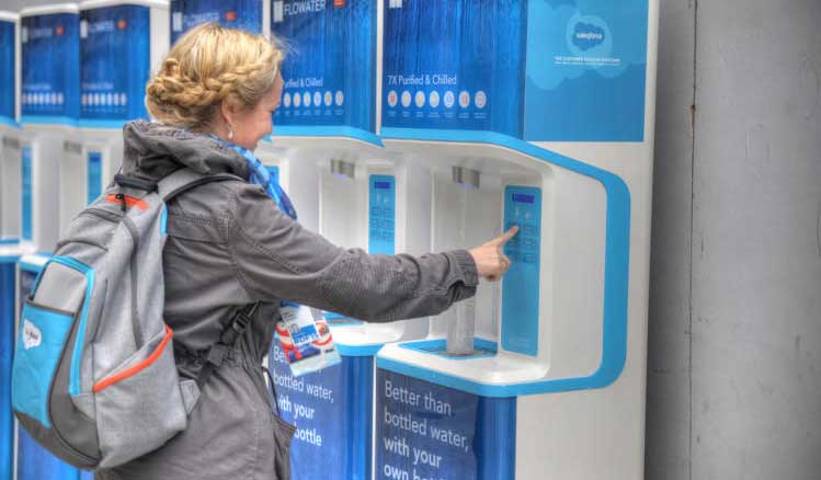 the woman with the bagpack fills a water bottle at the water filling stations