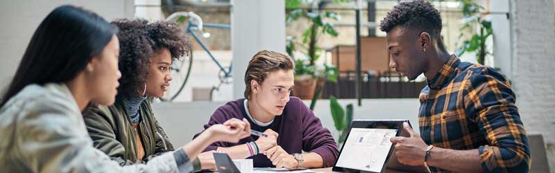 a group of students studying together at a table looking at laptop