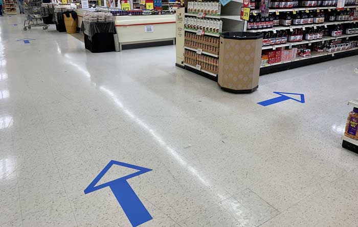 a blue arrow tape sign represents one-way aisles for social distancing in the store