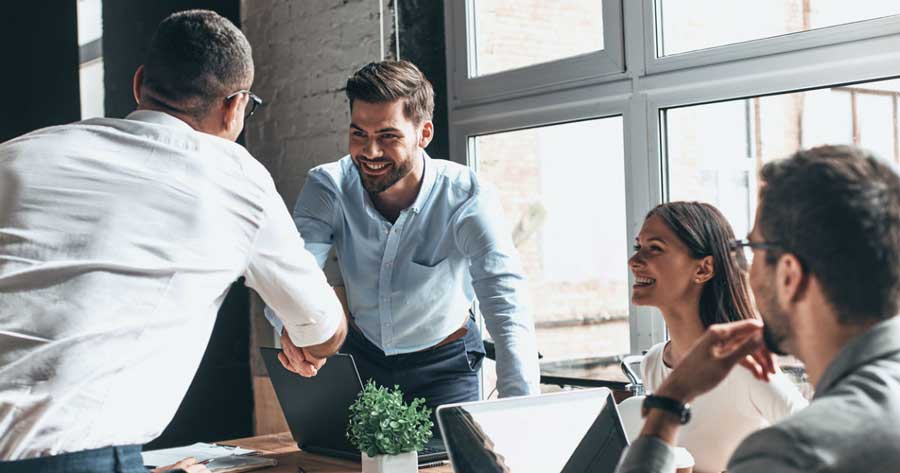 two men giving handshake while a smiling woman and a man wearing eyeglasses look at them