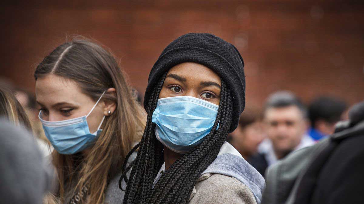 a crowd of people with two girls wearing blue face masks in the center