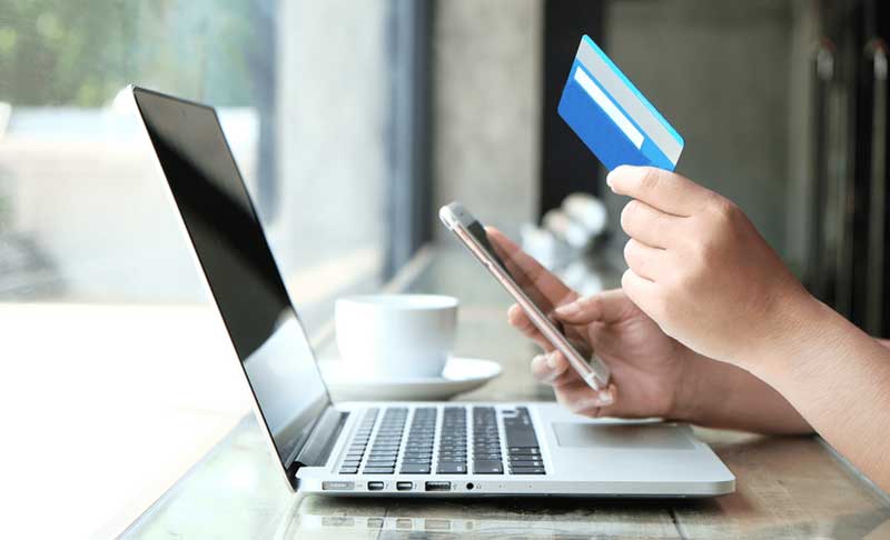 a picture of laptop and a hand carrying credit card and cellphone 