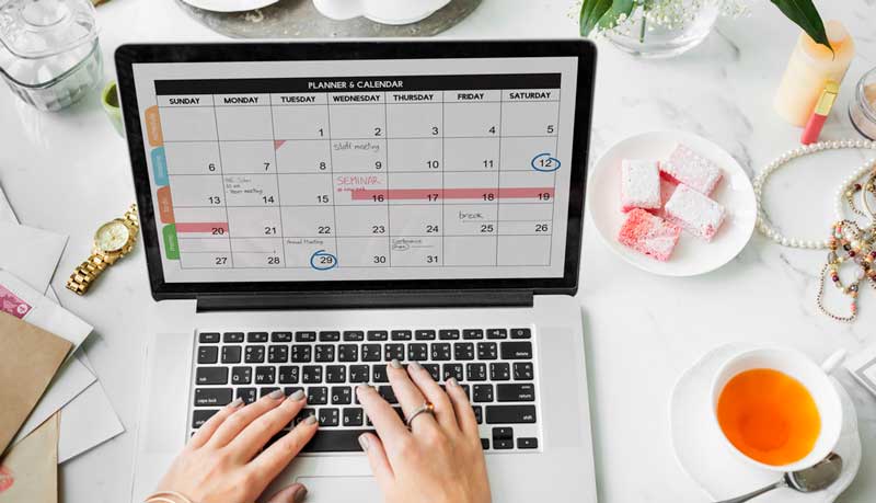 hands touching laptop keyboard and a calendar is shown on laptop screen