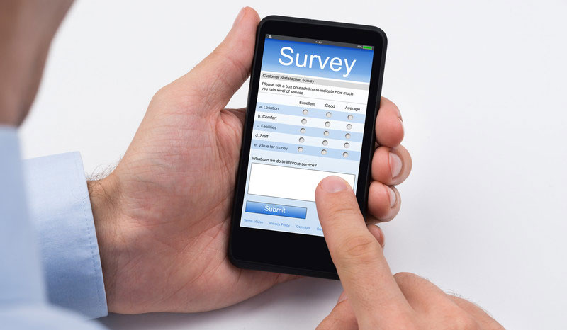 left hand holding a mobile phone with screen showing a survey form and index finger touching the screen