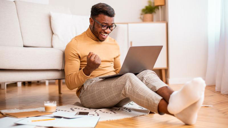 a man sitting on the ground in a yellow turtleneck looking at his computer